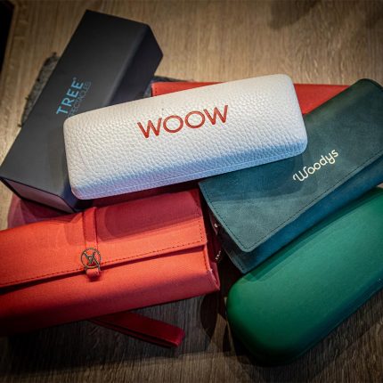 A selection of colourful glasses cases in red, green, teal and navy, with a pair of WOOW branded glasses resting on top